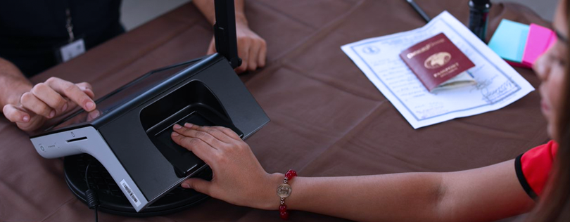 Poll worker uses VIU Desktop device to scan citizen's fingers at registration desk.