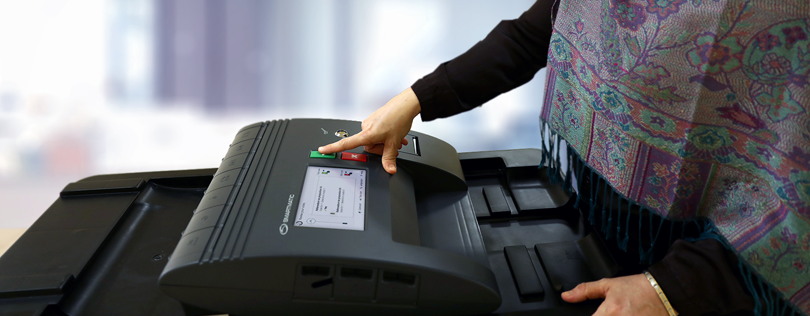 Female hand pushing the green button on precinct scanner to confirm her selection was cast correctly.